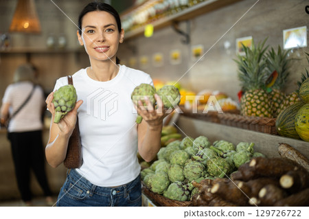 Positive woman shopping in organic food store, choosing artichokes 129726722