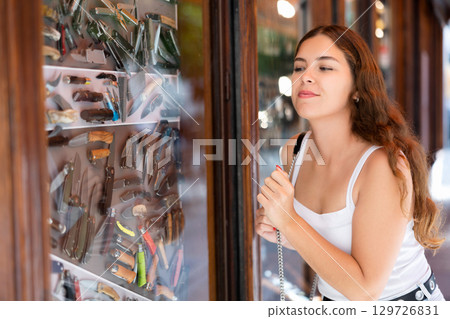 Young girl choosing souvenir knives in glass shop showcase 129726831