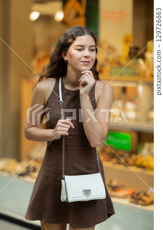 Beautiful young girl customer choosing something in souvenir shop during tourist trip in Spain Beautiful young girl customer choosing something in souvenir shop during tourist trip in Spain 129726863