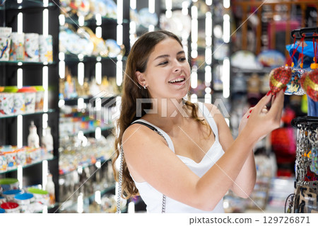 Cheerful young girl viewing funny items displayed in souvenirs shop 129726871