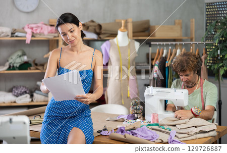 Young tailoress drawing sketches and man sewing in workshop Young tailoress drawing sketches and man sewing in workshop 129726887