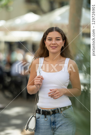 Cheerful girl walking at the street among architecture with bag Cheerful girl walking at the street among architecture with bag 129726901