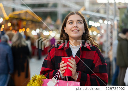 Happy girl with paper cup of coffee walking in Christmas fair 129726902