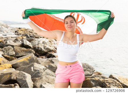 Pretty young girl holding the Iran flag in her hands on the seashore on sunny day 129726906
