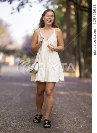 Cheerful girl in white dress walking along the street among architecture with bag Cheerful girl in white dress walking along the street among architecture with bag 129726931