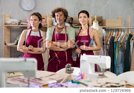 Portrait of sewing shop workers - man and two women posing in sewing shop interior Portrait of sewing shop workers - man and two women posing in sewing shop interior 129726966