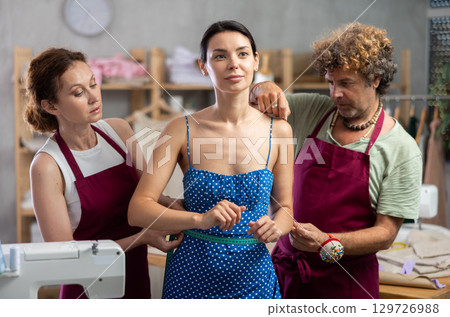 Female and male dressmakers measuring woman Female and male dressmakers measuring woman 129726988