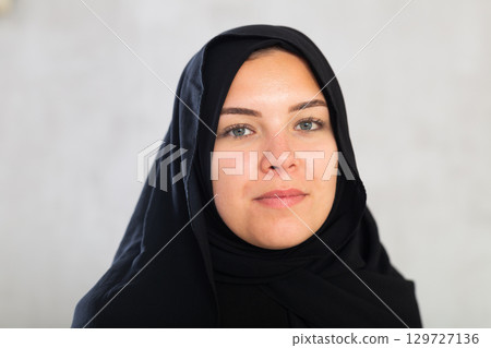 young calm Muslim woman in traditional hijab clothes poses on gray background. young calm Muslim woman in traditional hijab clothes poses on gray background. 129727136
