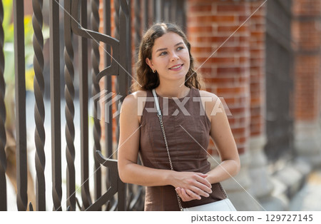 Young woman standing near the metal fence 129727145