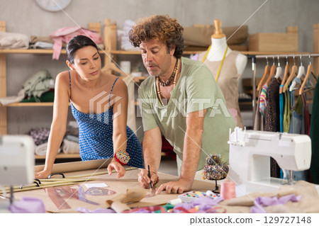 Female and male dressmakers drawing on paper in sewing studio 129727148