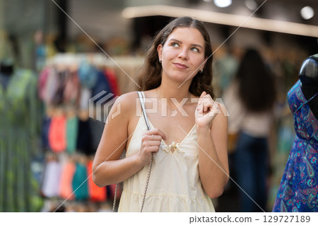 Young girl in white dress is looking for something at street market - looking at goods with interest Young girl in white dress is looking for something at street market - looking at goods with interest 129727189