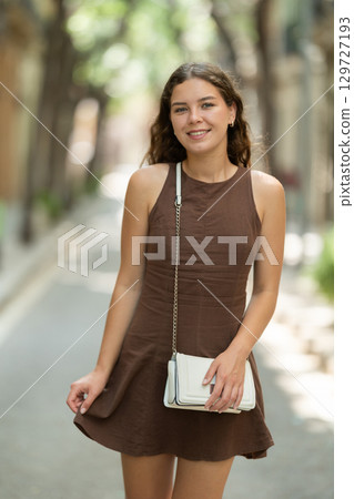 Beautiful smiling young lady wearing short dress walking shady tree lined street and relax in summer weather with sunshine outdoor 129727193