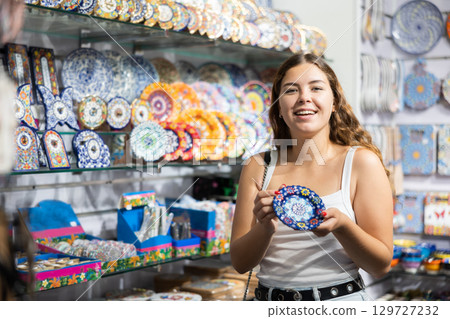 Female buyer holds in hands tests wall plate in memorable gifts shop 129727232