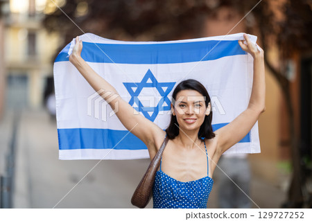 Young girl holding national flag of Israel, standing outdoors Young girl holding national flag of Israel, standing outdoors 129727252