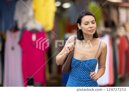 Young girl in blue dress is looking for something at street market - looking at goods with interest 129727253