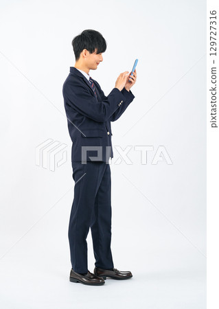A male student in uniform using a smartphone 129727316