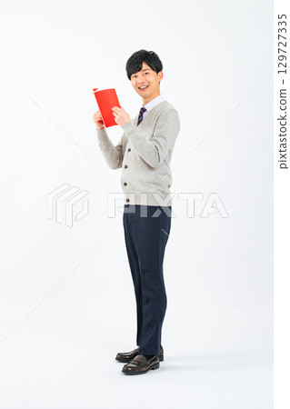 Full-body photo of a male student in uniform reading a red book 129727335