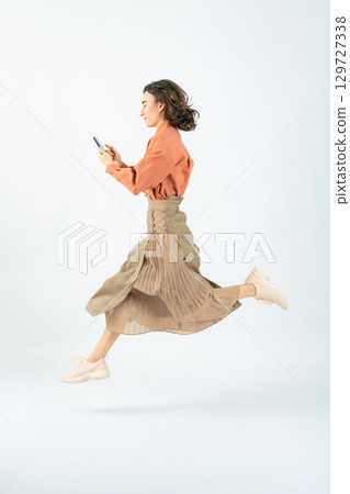 一名白人女子使用智慧型手機跳躍的全身照片 129727338