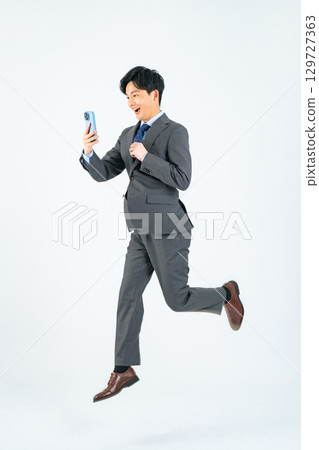 Full-body photo of a male business person jumping while looking at his smartphone Full-body photo of a male business person jumping while looking at his smartphone 129727363