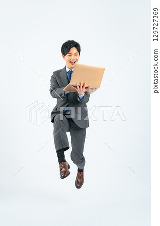 Full body photo of a young businessman jumping with a laptop 129727369