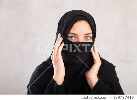 Muslim woman with face covered with burka holds thin fabric of yashmak with her hands 129727419