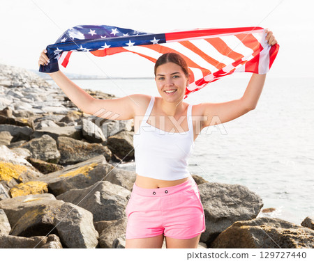 Happy girl waving the USA flag on the seashore on sunny day Happy girl waving the USA flag on the seashore on sunny day 129727440
