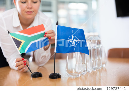Young woman putting South Africa and NATO flags on table in office 129727441