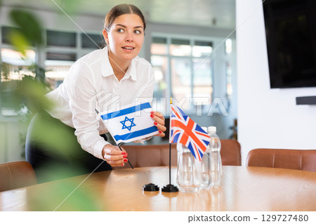 Businesswoman preparing table in meeting room for Anglo-Israeli negotiations 129727480