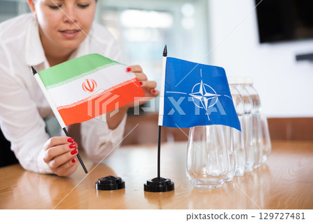 Woman secretary prepares an office for negotiations - she places flags of NATO (OTAN) and Iran table Woman secretary prepares an office for negotiations - she places flags of NATO (OTAN) and Iran table 129727481