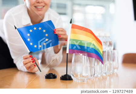 Young woman puts EU and LGBT flags on table in office Young woman puts EU and LGBT flags on table in office 129727489
