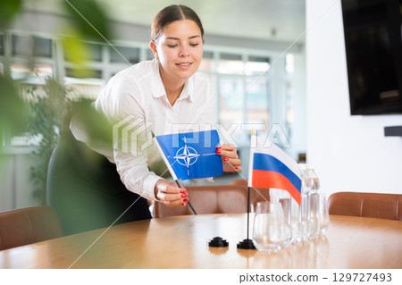 Young lady sets miniatures flags of Russia and NATO before international negotiations Young lady sets miniatures flags of Russia and NATO before international negotiations 129727493