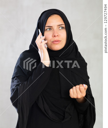 Young woman dressed in traditional islamic clothes looking up something on her phone 129727494