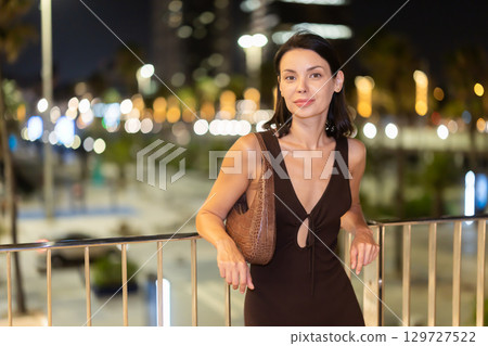 Young woman leaning on metal railing against background of blurred city lights Young woman leaning on metal railing against background of blurred city lights 129727522