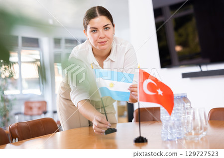 Positive young woman putting flag of Argentina on the table with flag of Turkey in conference room Positive young woman putting flag of Argentina on the table with flag of Turkey in conference room 129727523