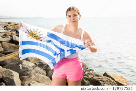 Young woman on coast posing with flag of Uruguay 129727525
