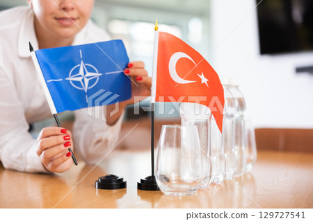 Little flag of Turkey on table and flag of NATO put next to it by young woman Little flag of Turkey on table and flag of NATO put next to it by young woman 129727541