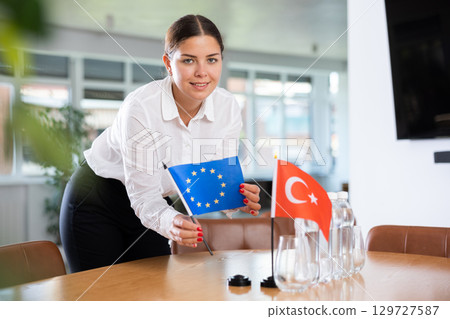 Female secretary places flags of the Turkey and European Union flag on the table before negotiations of top political figures 129727587