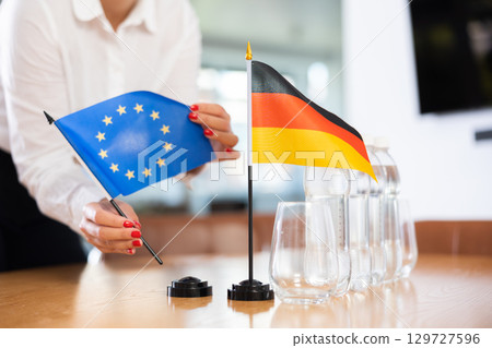 Little flag of Germany on table and flag of European Union put next to it by young woman Little flag of Germany on table and flag of European Union put next to it by young woman 129727596