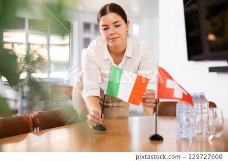 Young female assistant putting up swiss and italian flags on table for international negotiations Young female assistant putting up swiss and italian flags on table for international negotiations 129727600
