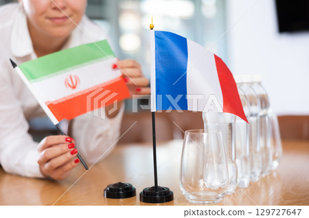 Woman secretary prepares the negotiating table - arranges flags of France and Iran Woman secretary prepares the negotiating table - arranges flags of France and Iran 129727647