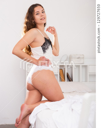 Girl in white lace undershirt and panties posing in bedroom Girl in white lace undershirt and panties posing in bedroom 129727650