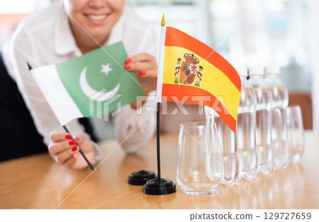 Young woman putting flags of Pakistan and Spain on table in office 129727659