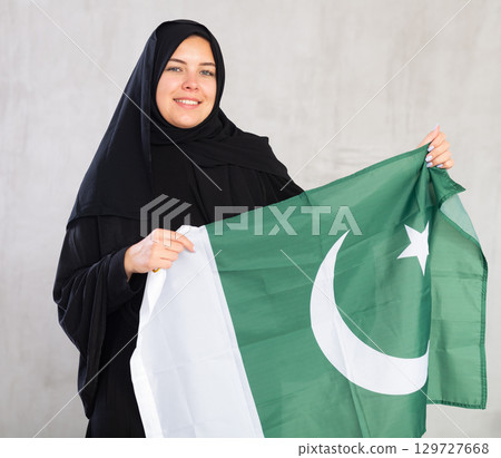 Balanced smiling Muslim woman in traditional black hijab holds flag of Pakistan Balanced smiling Muslim woman in traditional black hijab holds flag of Pakistan 129727668