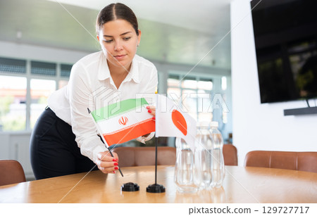 Positive young woman putting little flag of Iran on table next to the flag of Japan 129727717