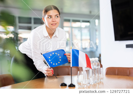 Young woman puts EU and France flags on table in office 129727721