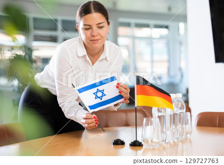 Positive young woman putting little flag of Israel on table next to the flag of Germany 129727763