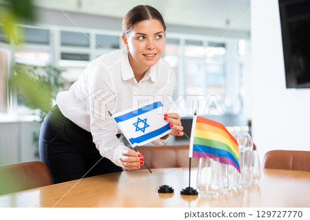 Woman placing flags of Israel and LGBT community on table in office 129727770