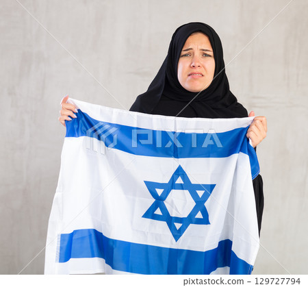 upset Muslim woman in traditional black hijab holds flag of Israel upset Muslim woman in traditional black hijab holds flag of Israel 129727794