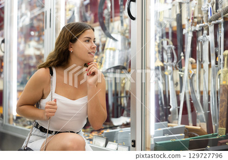 Interested young woman viewing various swords placed on display case 129727796