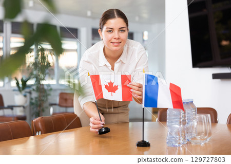 Employee of delegation prepares negotiating table - sets up flag of Canada and France Employee of delegation prepares negotiating table - sets up flag of Canada and France 129727803